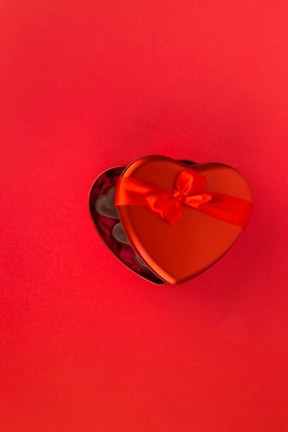 Red heart-shaped box with chocolate candy on red background