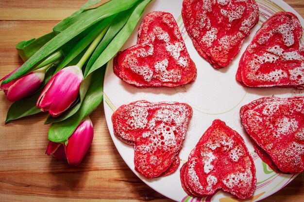 Red heart shaped pancakes made with love for valentines day and tulips on wooden background