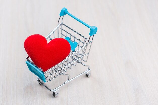 Red heart in the shopping cart on the wooden floor