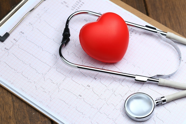 Red heart with stethoscope and electrocardiogram on wooden background