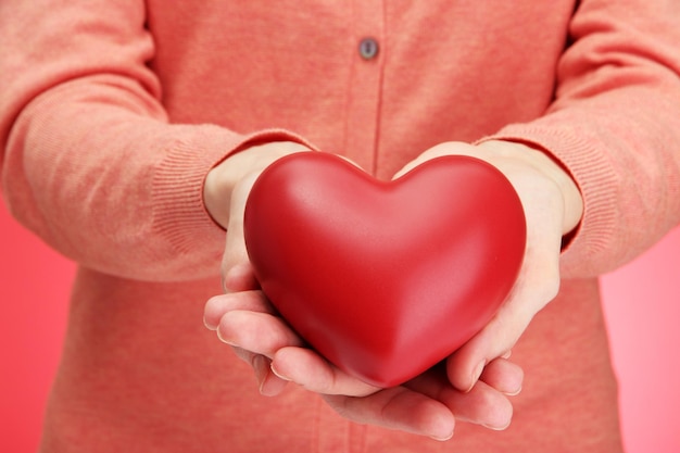 Red heart in woman hands, on red background