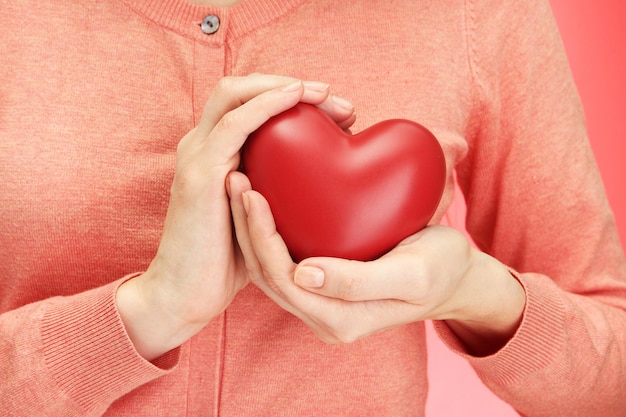 Red heart in woman hands, on red background