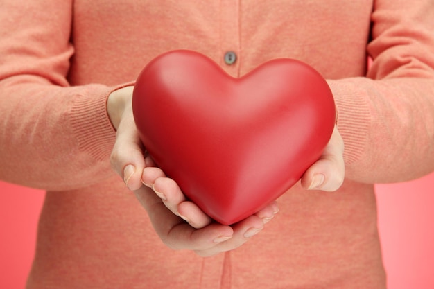 Red heart in woman hands, on red background