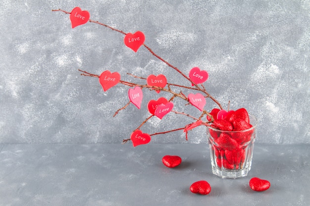 Red hearts with an inscription Love hang on branches on a gray concrete background. Love tree.