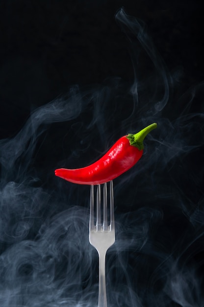 Red Hot Chili Pepper on Fork with Smoke on Black Background.