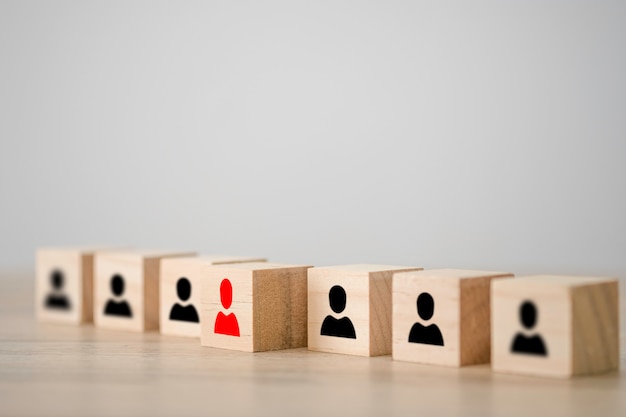 Red human icon on a wooden cube in front of other black human icon wooden cubes. Leadership and different thinking concept.