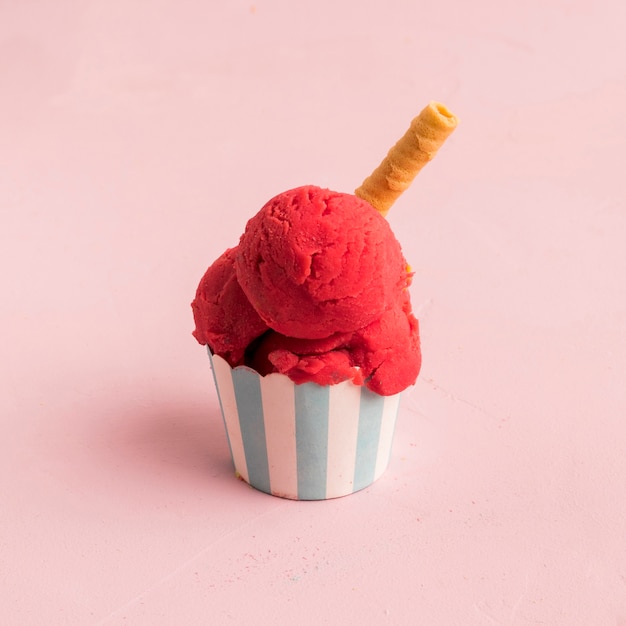 Red ice cream scoop with waffle straw in striped bowl