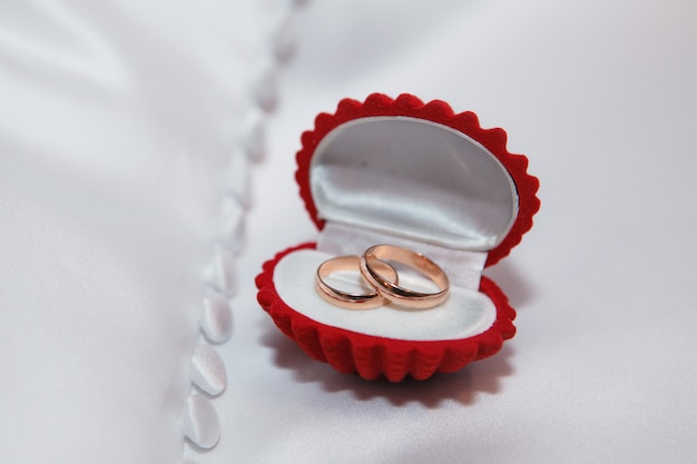 Red jewelry box with gold wedding rings on the white fabric