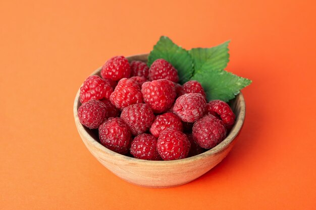 Red juicy raspberries in a wooden bowl on an orange background.