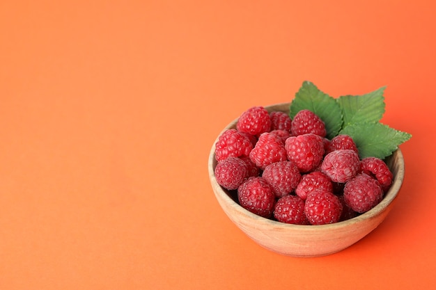 Red juicy raspberries in a wooden bowl on an orange background.