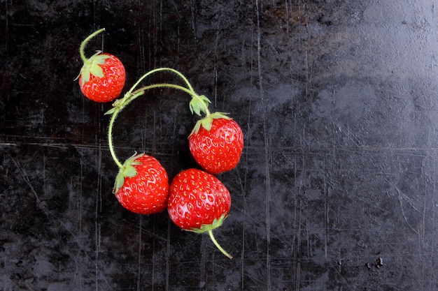 Red juicy sweet strawberries with twigs on a black background Closeup of red berries Healthy food concept