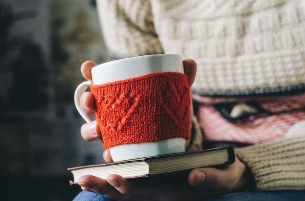 Red Knitted woolen cup with heart pattern in female hands.