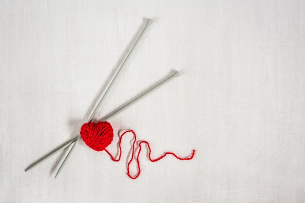 Red knitting yarn with needles and heartbeat on white wooden background.