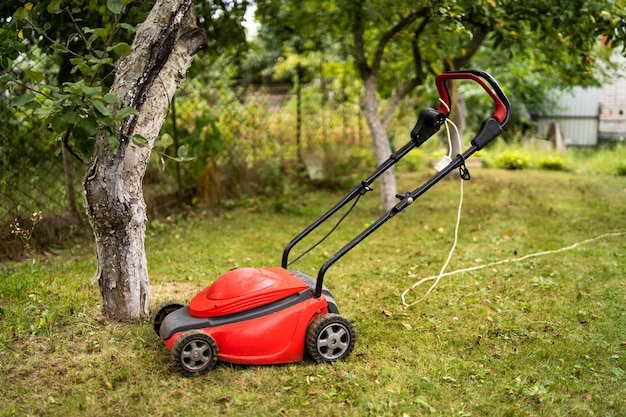 Red lawn mower outdoor in the backyard. green grass and fruit trees background