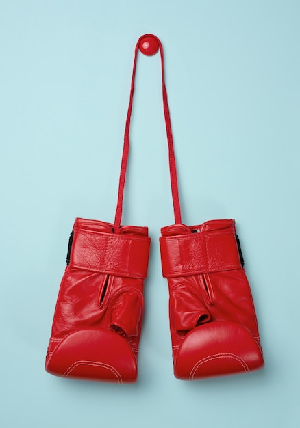 Red leather boxing gloves hanging on a cord blue background