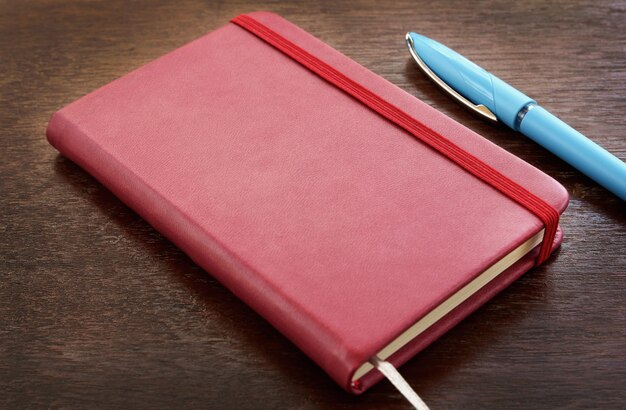 Red leather notebook with pens on wooden table.