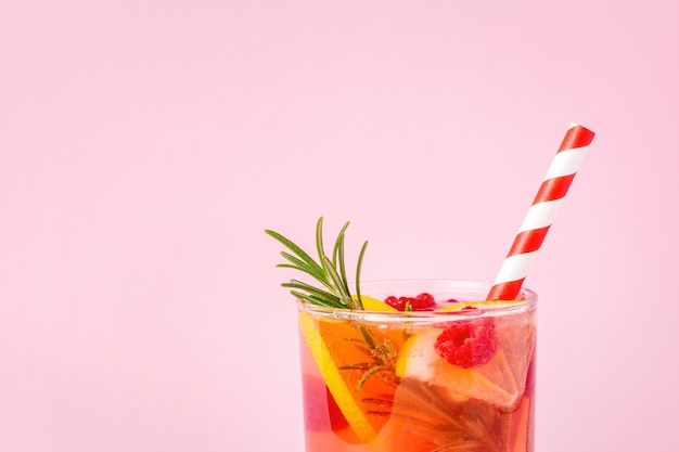 Red lemonade with lemon and raspberry decorated with rosemary on pink background. Summer cocktail with citrus fruit and berries.