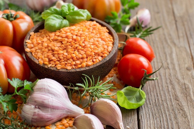 Red lentils in a bowl with tomatoes, garlic and herbs on wood