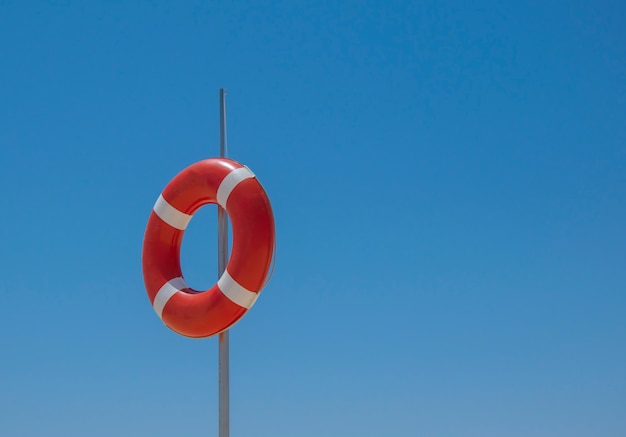 Red liifebuoy on the pole on blue sky background