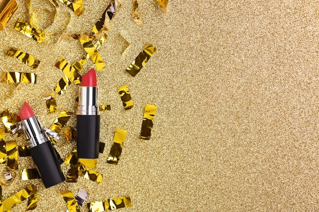 Red lipstick on a shiny golden background with glitter top view. Women's beauty cosmetic product for professional lip makeup.