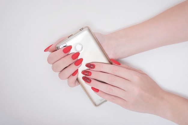 Red manicure with a pattern. Smart phone in female hand. White 