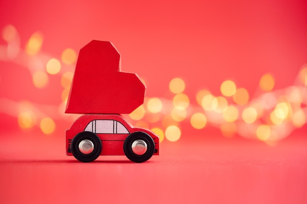 Red model of car delivering red paper heart on red background Creative greeting card for Saint Valentine day