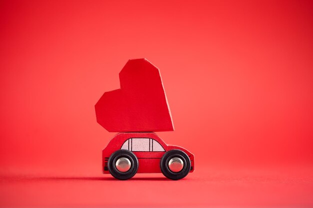 Red model of car delivering red paper heart on red background Creative greeting card for Saint Valentine day