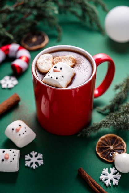 Red mug with hot chocolate and melted marshmallow snowman green festive background