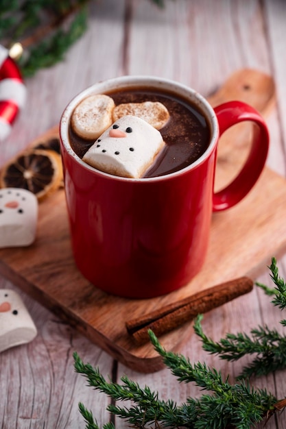 Red mug with hot chocolate and melted marshmallow snowman rustic wooden festive background