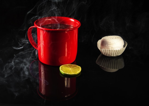 Red mug with hot tea and white marshmallows on black mirror