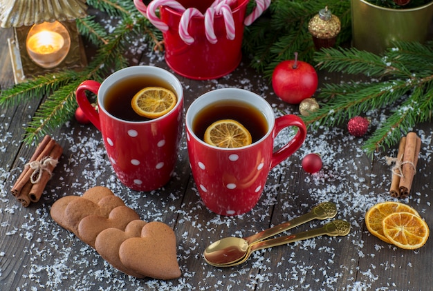 Red mugs with tea, caramel cane, heart-shaped cookies, an apple, a lantern with a candle