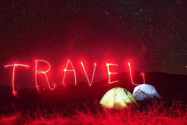 Red neon travel word Two iluminated tents under stars at mountains at night