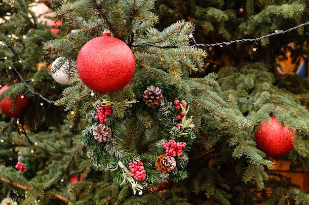 Red New Year balls and garland on a branches of natural Christmas tree outdoors at sunny summer day