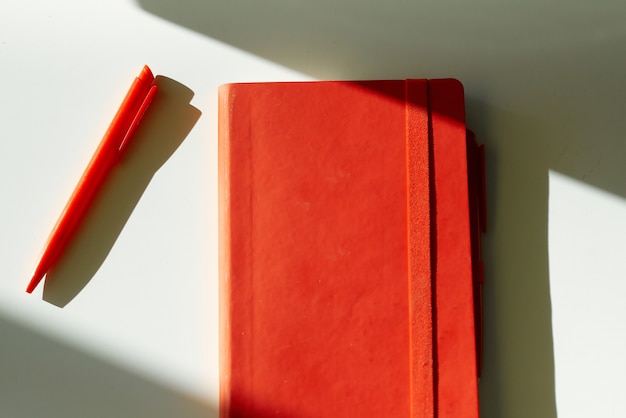 Red notebook note pen sun light white table