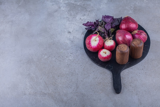 Red onions, radishes and fresh basil on black cutting board.