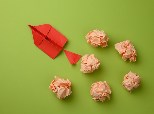 Red paper airplane and crumpled paper balls on a green surface, top view. The concept of finding innovative ideas, the right solutions. Elimination of mistakes and a leap forward for the leader