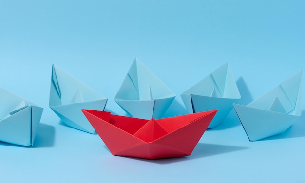 A red paper boat stands in front of a group of blue paper boats a confrontation