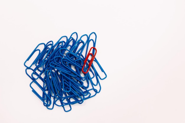 A red paper clip stands out against a background of blue paper clips.