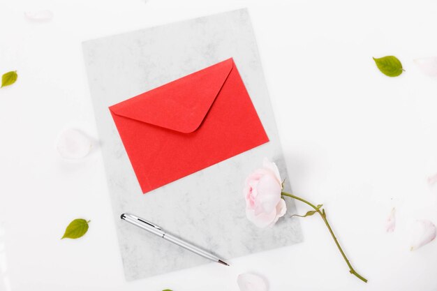 Red paper envelope with blank note and Valentines pink rose on white background Flat lay top view Romantic love letter