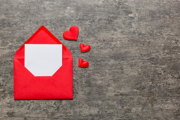 Red paper envelope with empty white card and heart on colored background top view valentines day concept