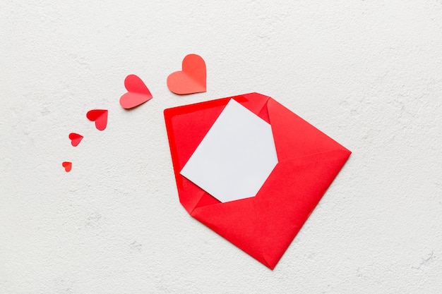 Red paper envelope with empty white card and heart on colored background top view valentines day concept