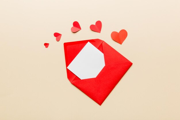 Red paper envelope with empty white card and heart on colored background top view valentines day concept