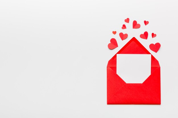 Red paper envelope with empty white card and heart on colored background top view valentines day concept