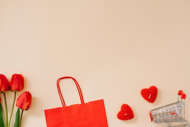 A red paper shopping bag a bouquet of tulips and a shopping cart Holiday discounts for Valentine's Day with space copying Banner on beige background