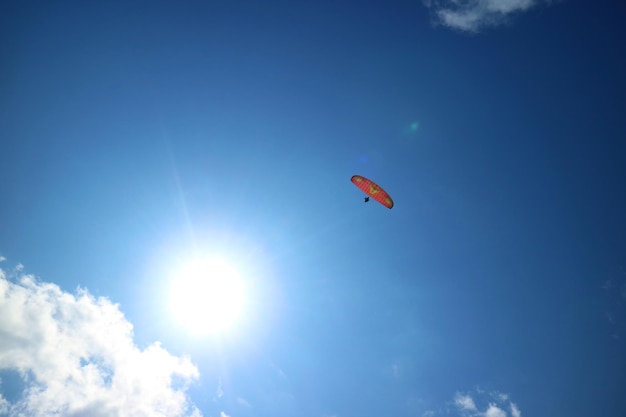 Red Paraglider Flying in the Blue Sky with the Dazzling Sun