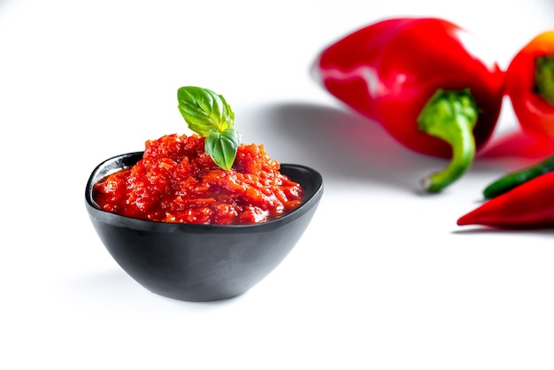 Red paste ajvar of red sweet peppers on white background with ingredients for cooking