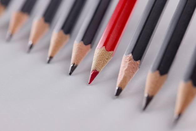 Red pencil that stands out from many identical black pencils on gray background