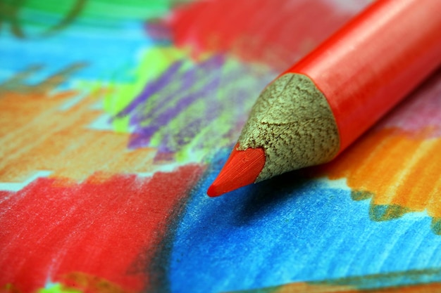 A red pencil with a red tip sits on a colorful table.