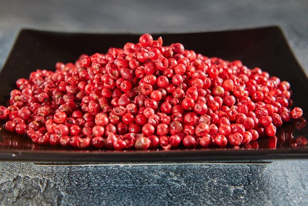 Red peppercorns on black plate with reflection