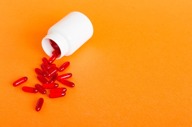 Red pills spilled around a pill bottle Medicines and prescription pills flat lay background Red medical capsules